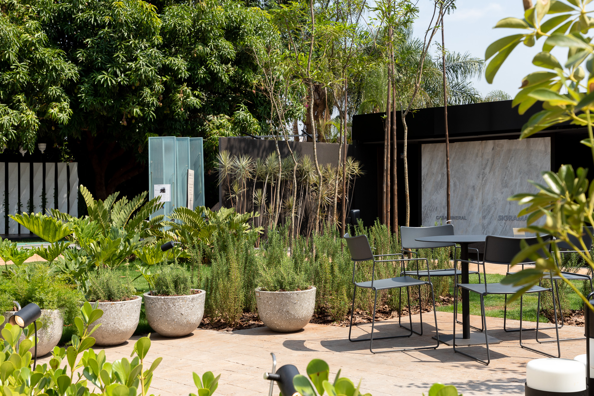 Mônica Costa Paisagismo - Jardim dos Alecrins. O perfume dos alecrins é protagonista na praça central da CASACOR Ribeirão Preto 2022. Nesse jardim de sensações de Mônica Costa, é o aroma que impacta o visitante ao primeiro contato. Em seguida percebe-se a leveza que o espaço proporciona, assim como o equilíbrio na composição de texturas. Mônica apresenta um projeto com plantas baixas, para manter a perspectiva da arquitetura das construções próximas. Para ela, o desafio é sempre criar uma conexão harmônica entre a natureza e as novas materialidades. “Aliado à arquitetura como ponto de partida de um projeto, o paisagismo integra essa relação naturalmente desde sua criação, gerando um movimento de colaboração entre os dois mundos”. A iluminação, outra ótima surpresa do espaço, é assinada por Filippo Giorgi (Lucenera).