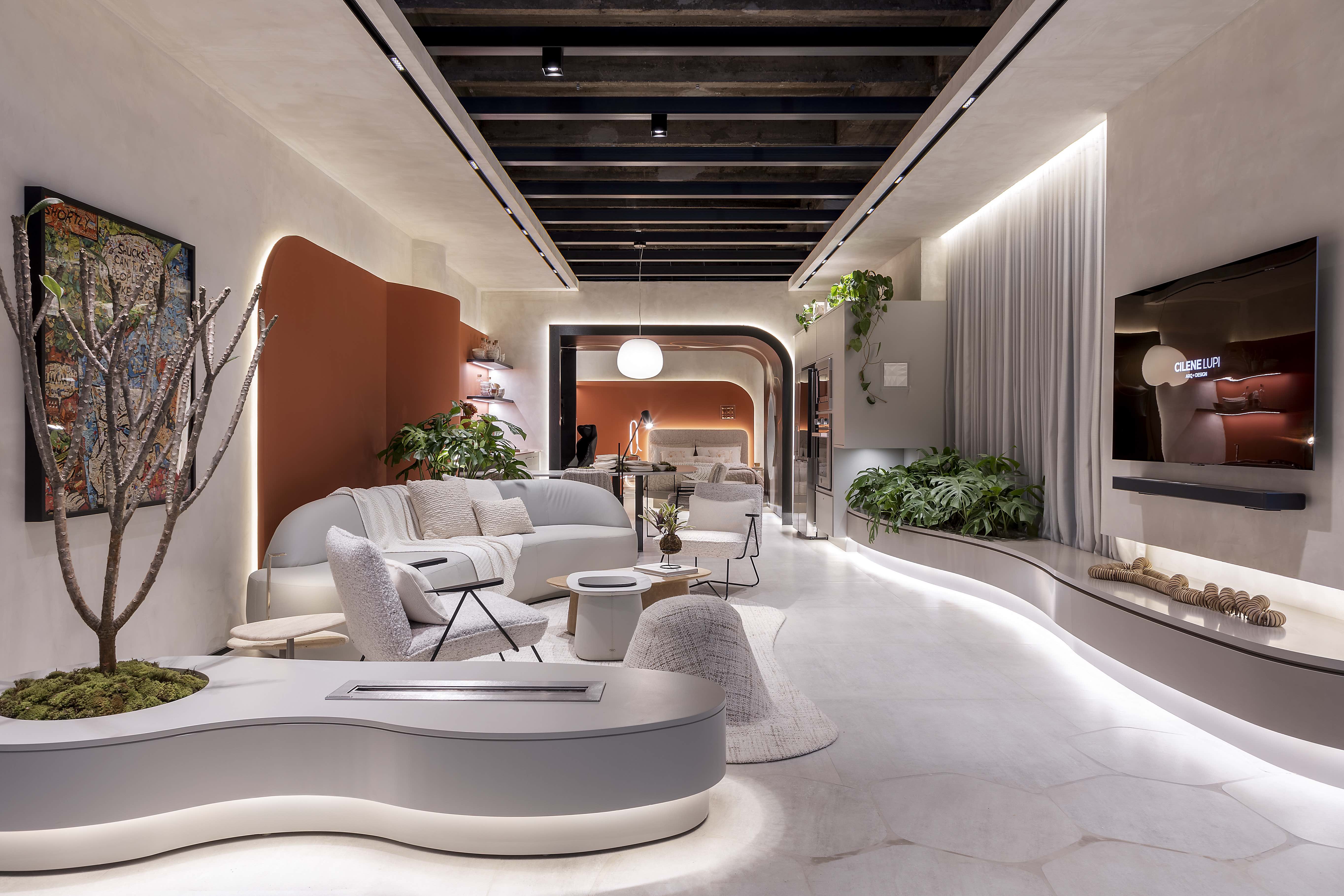 Cilene Lupi - Um lar para apertar o pause. Projeto da CASACOR São Paulo 2023. Na foto, loft com quarto, sala e cozinha. Móveis curvos, tv, lareira e paredes laranjas.