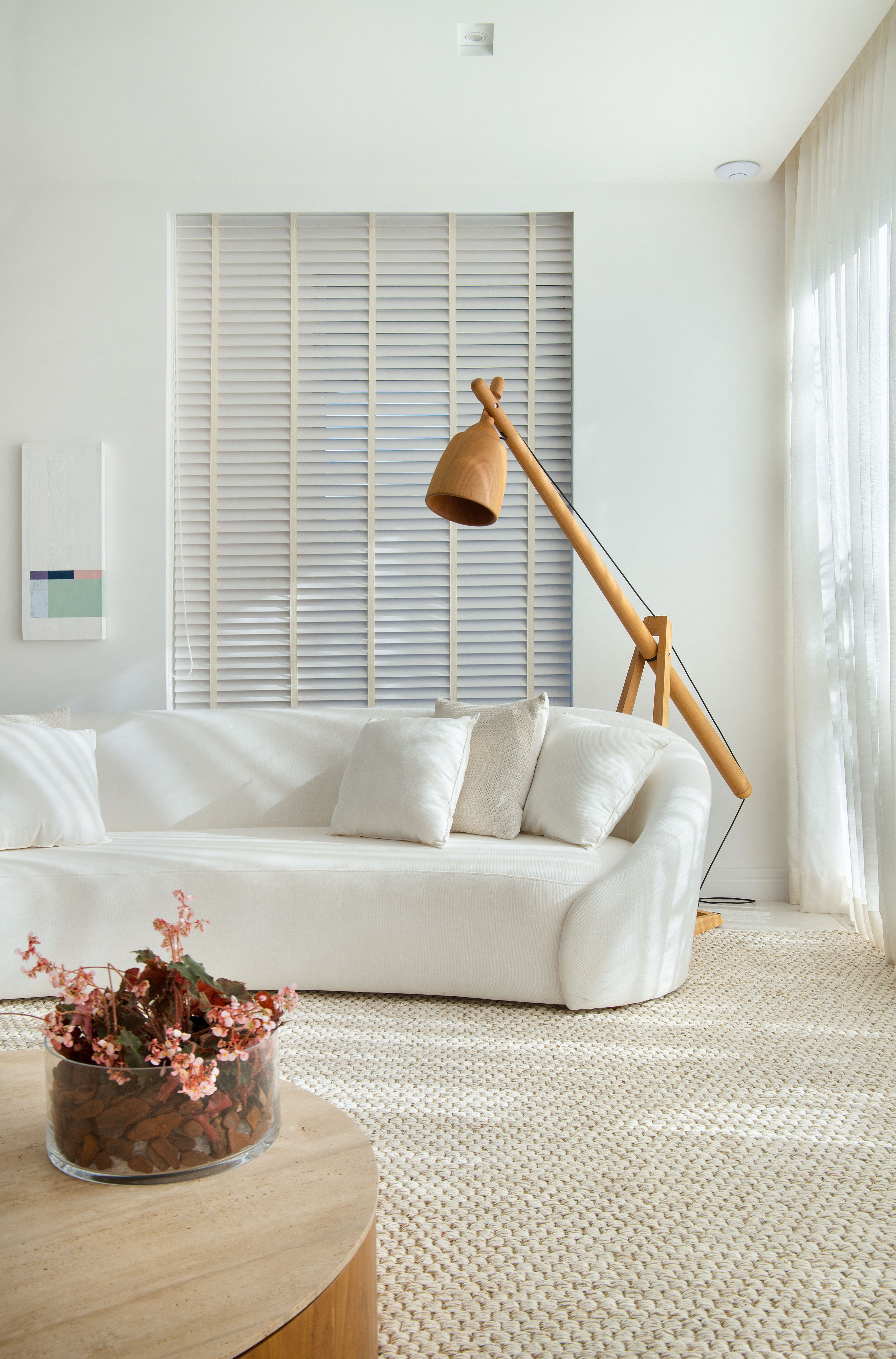 Madeira e branco marcam o décor minimalista deste apê de 450 m². Projeto de Diego Raposo e Manuela Simas, do escritório Diego Raposo + Arquitetos. Na foto, sala com decor neutra, sofa curvo e luminaria de piso.