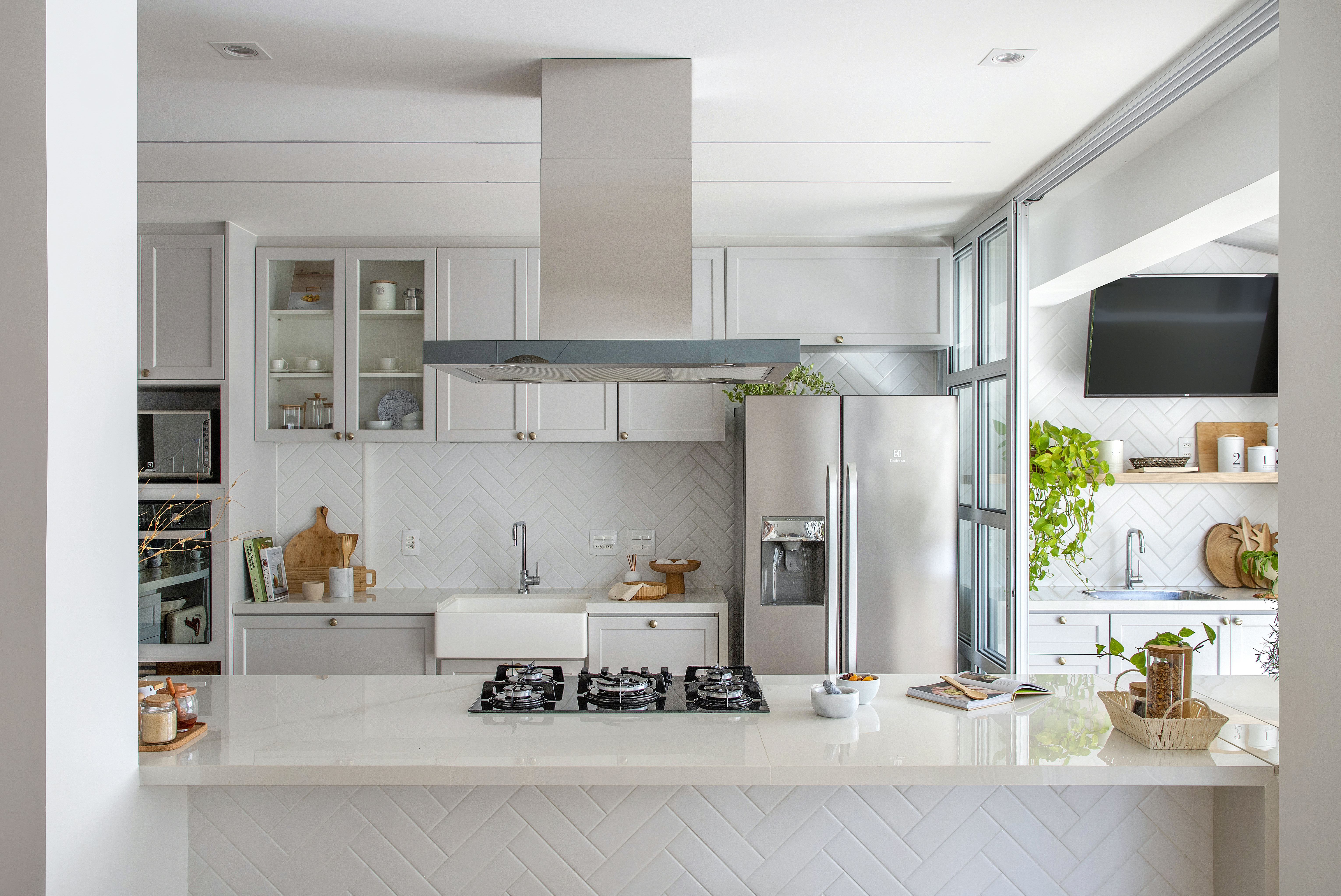 Duplex de 210 m² ganha décor na cor branca no estilo clássico e boho. Projeto de Amanda Miranda. Na foto, cozinha com marcenaria cinza, torre quente e backsplash em espinha de peixe.