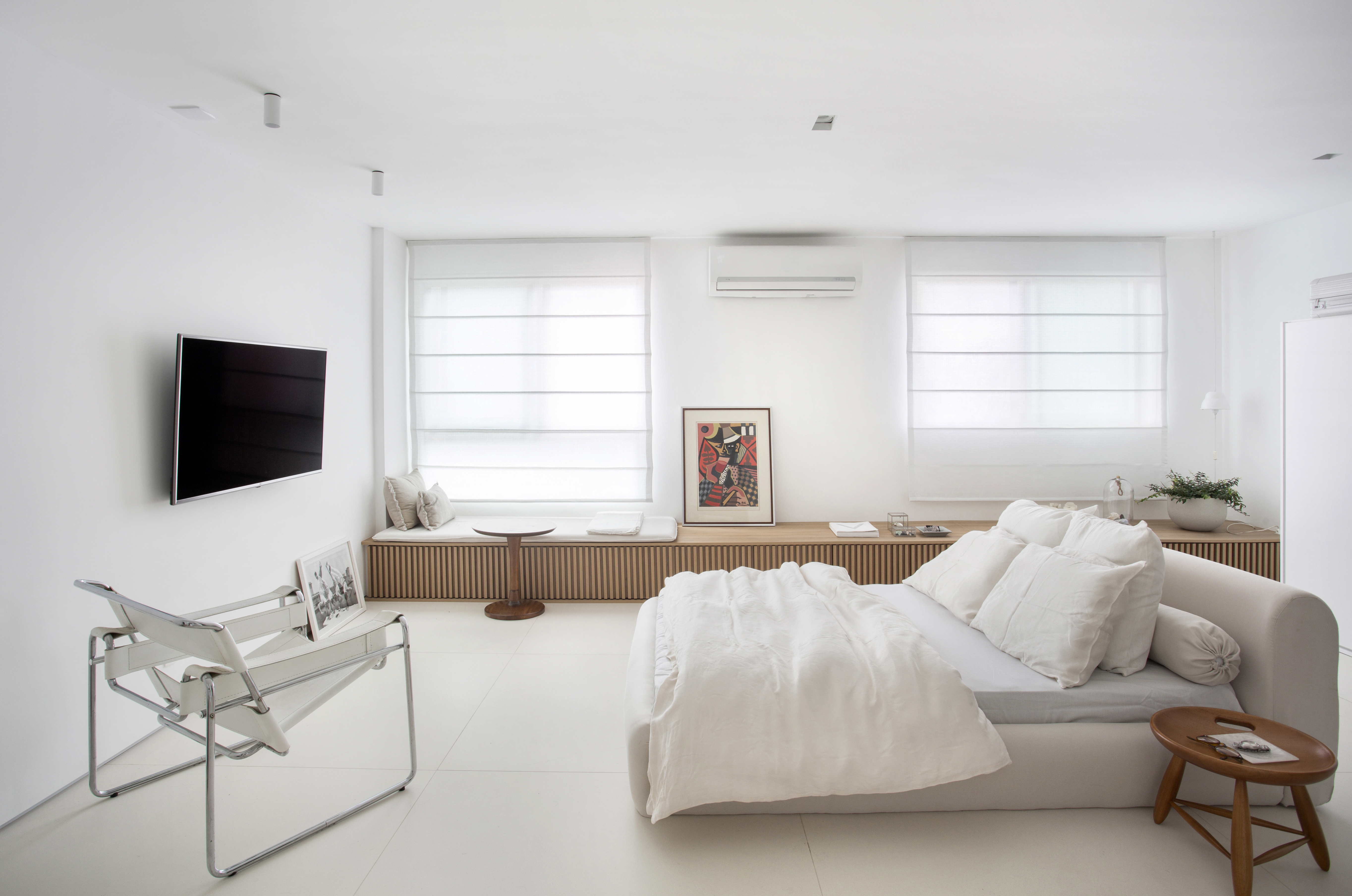 Loft de 40 m² ganha projeto minimalista que une branco e madeira. Projeto de Diego Raposo e Manuela Simas. Na foto, quarto com tv e banco ripado.