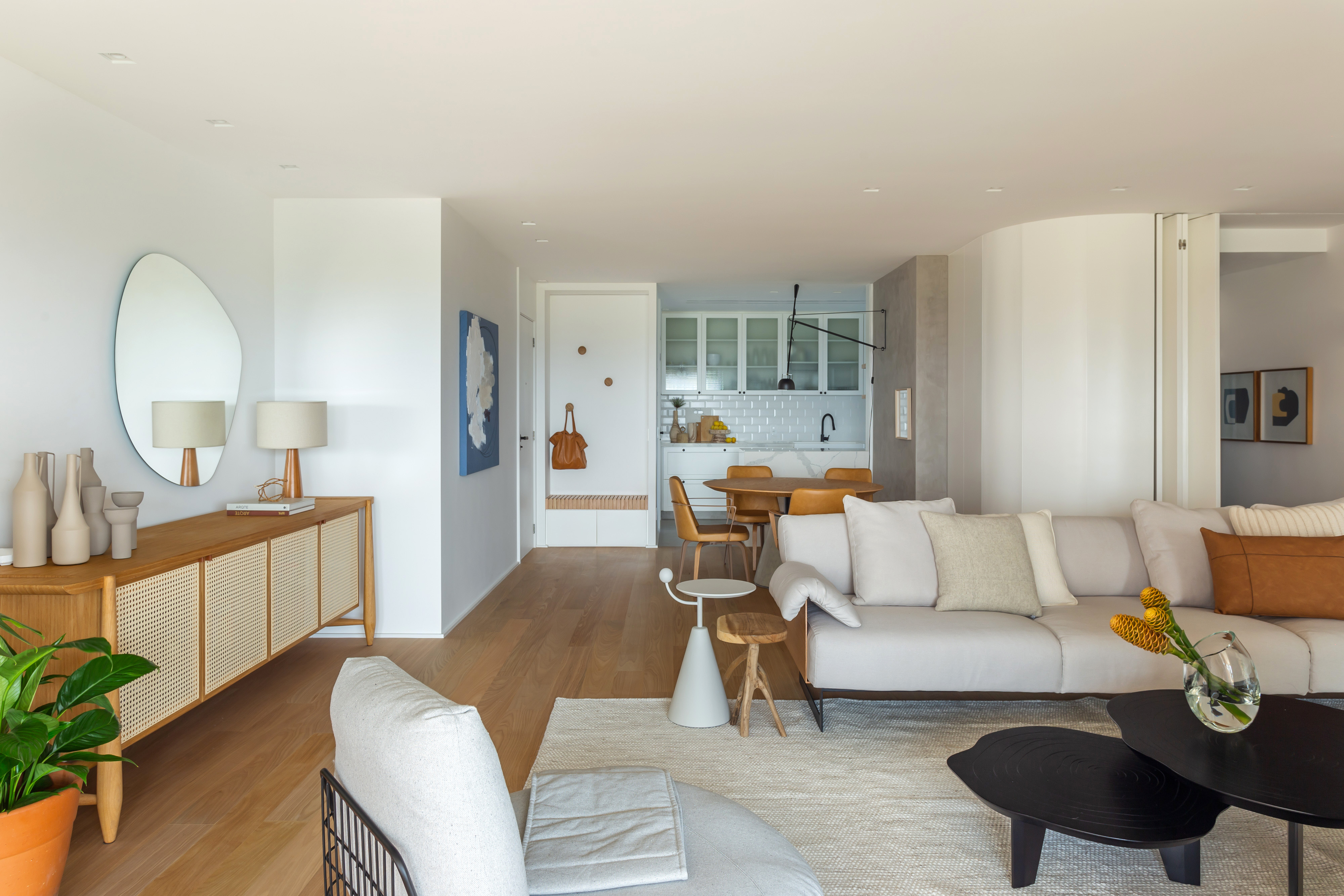 Apê na Barra da Tijuca ganha décor minimalista, mas muito aconchegante. Projeto de A+G Arquitetura, Na foto, sala de estar integrada com cozinha com decor claro, aparador e sofás.