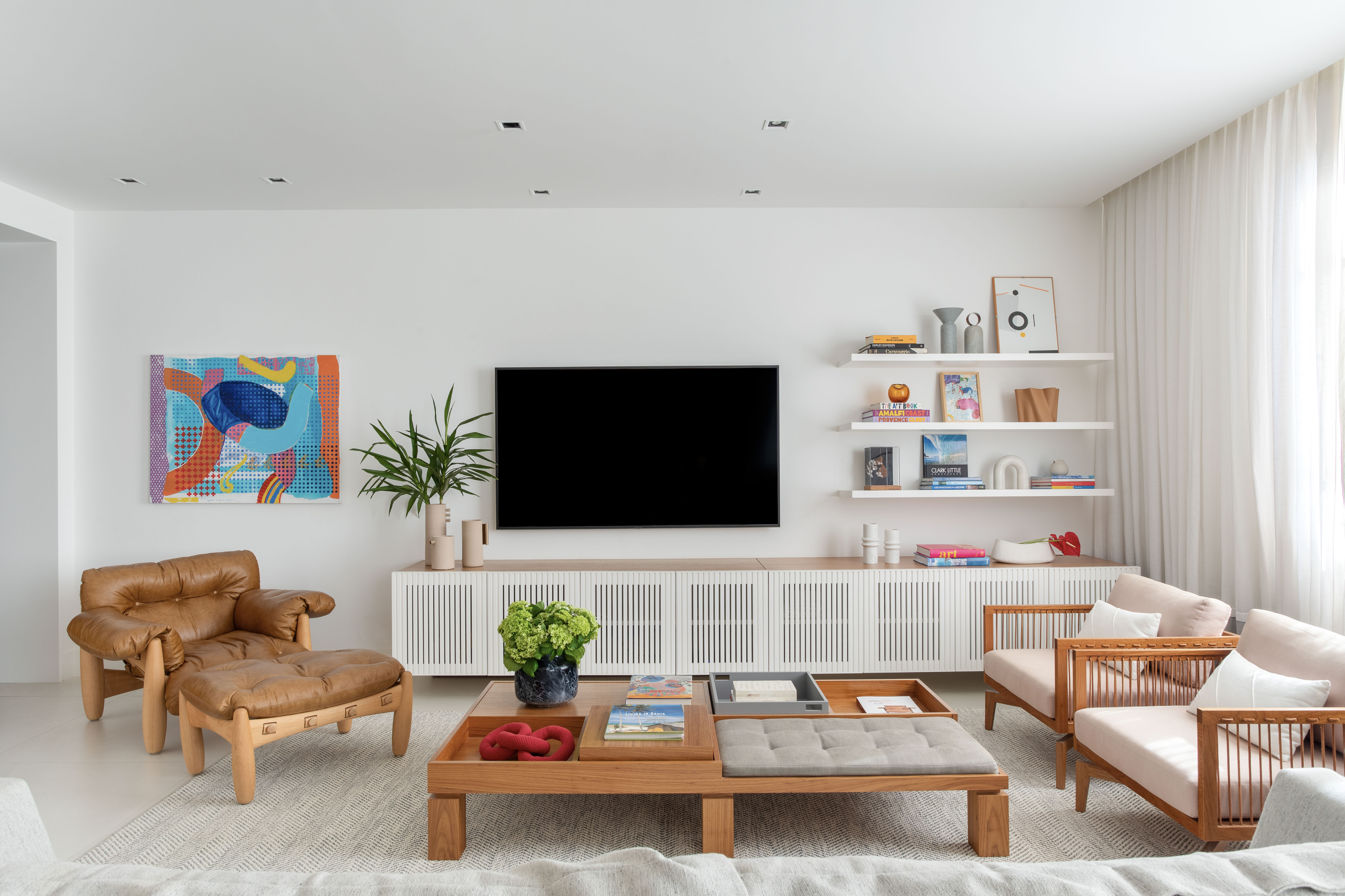 Décor atemporal, layout aberto e design brasileiro marcam apê de 210 m². Projeto de Bezamat Arquitetura, Na foto, sala de estar com tv, aparador ripado e quadros.