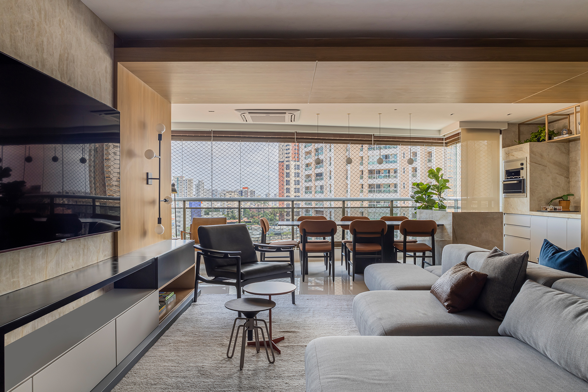 Romário Rodrigues cria projeto contemporâneo em apê de 220 m² no Ceará. Na foto, sala integrada à varanda com tv, churrasqueira e sofás.
