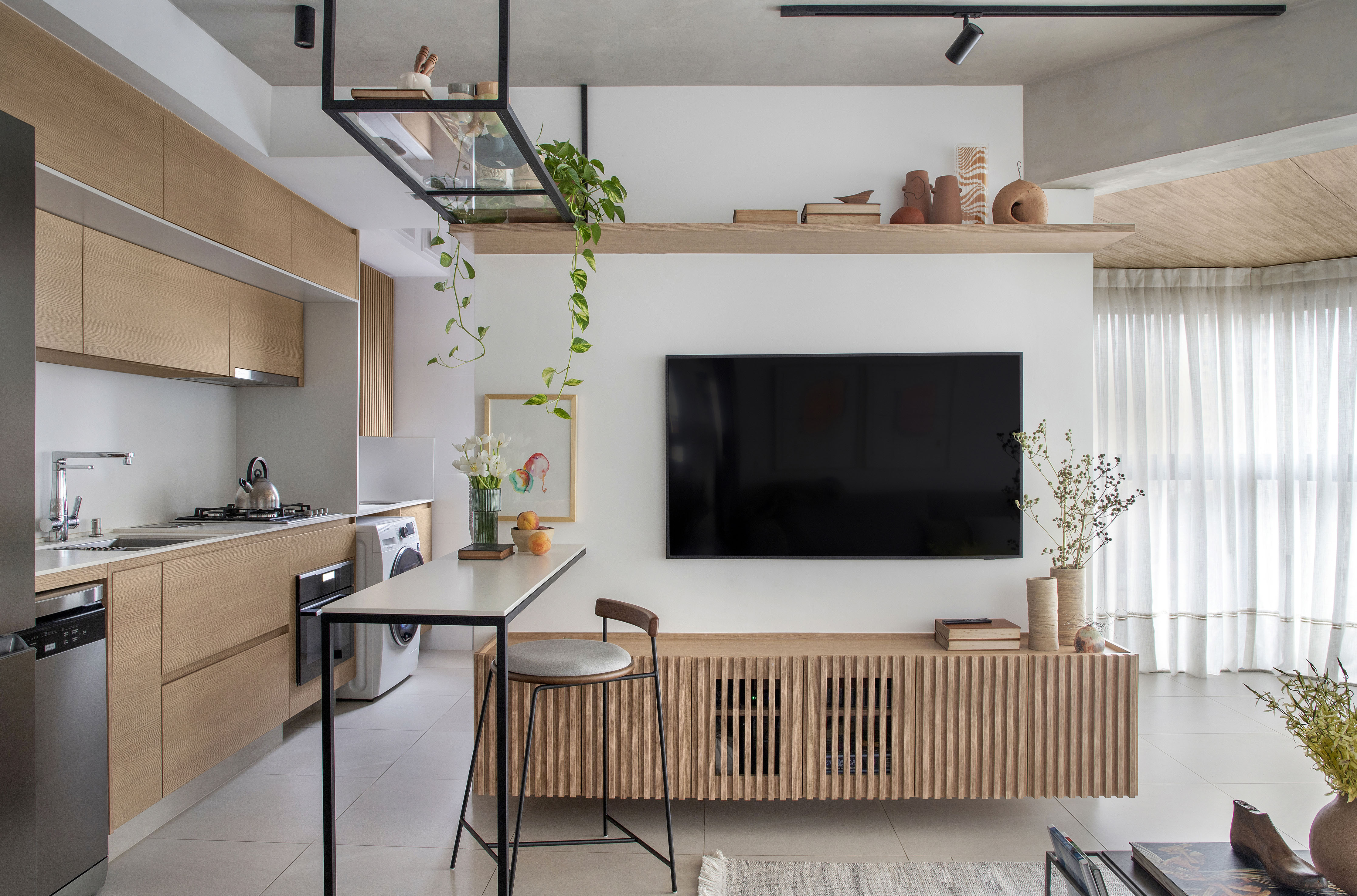 Reforma em apê de 105 m² cria lar aconchegante para mãe e filha. Projeto de Rafael Ramos. Na foto, cozinha integrada com bancada e prateleiras. Tv e rack ripado.