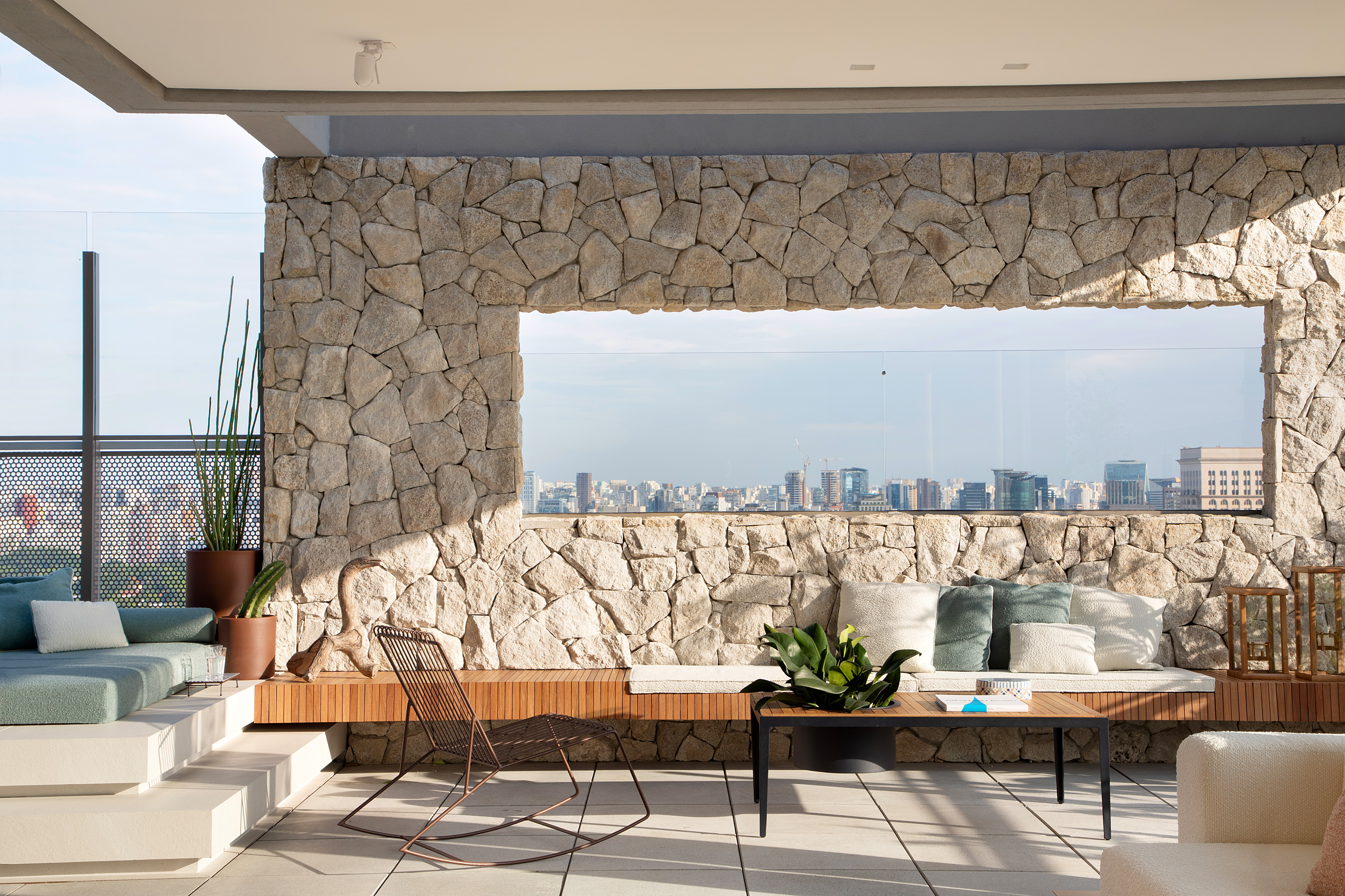 Skyline de São Paulo é emoldurado em apê assinado por Sabugosa Arquitetura. Na foto, terraço com muro de pedra, banco e piscina.