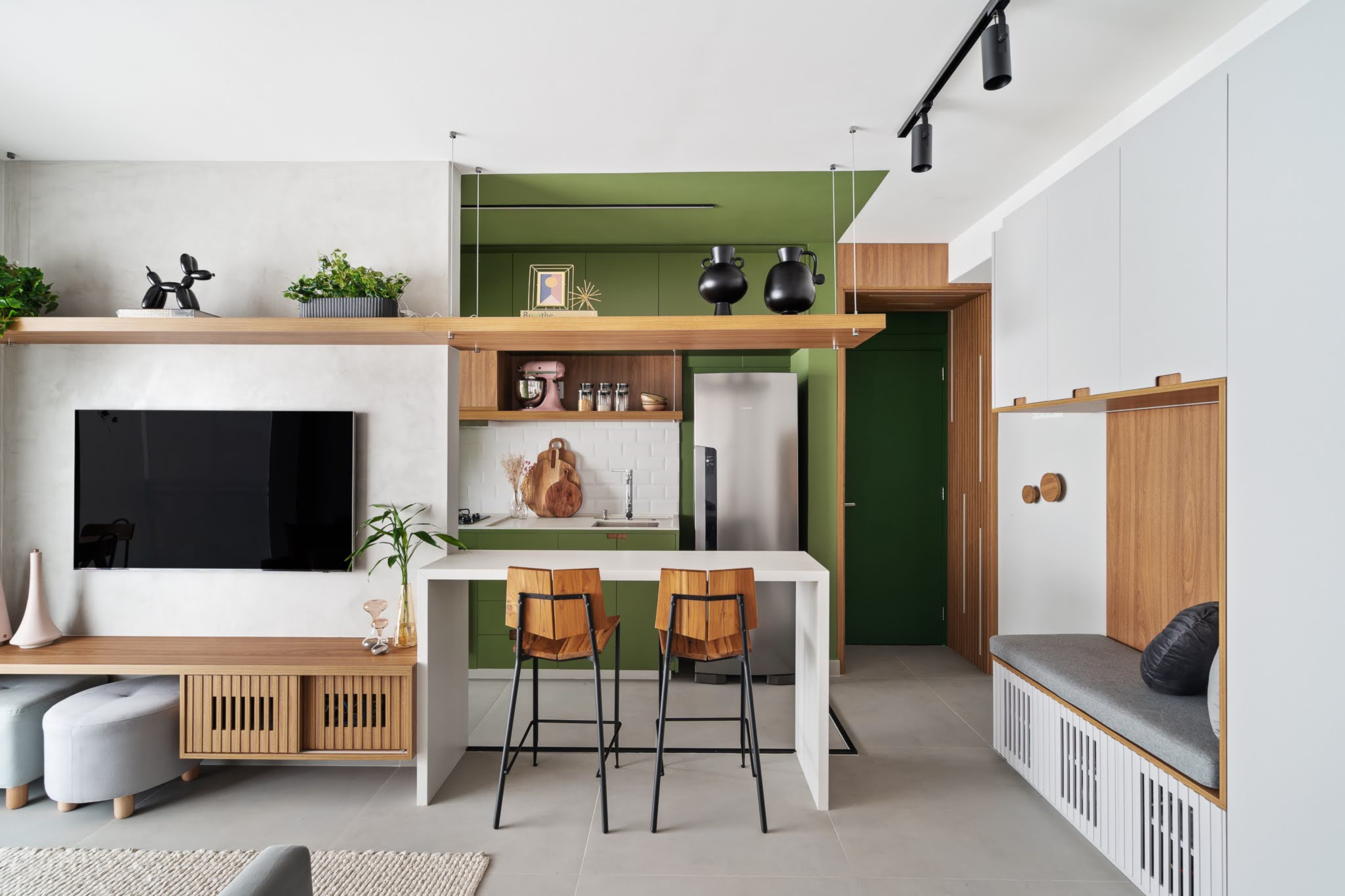 Cozinha verde e detalhes coloridos personalizam apê de 49 m². Projeto de Natalia Salla. Na foto, sala integrada com cozinha, marcenaria verde, parede de tijolinhos e sofá cinza.