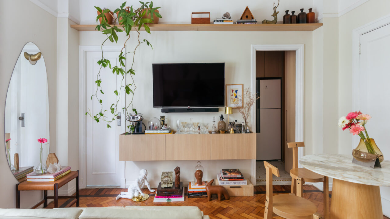 Conheça o apartamento de 42 m² do arquiteto Rodolfo Consoli em Copacabana. Na foto, sala com prateleira, tv, espelho orgânico e varanda.