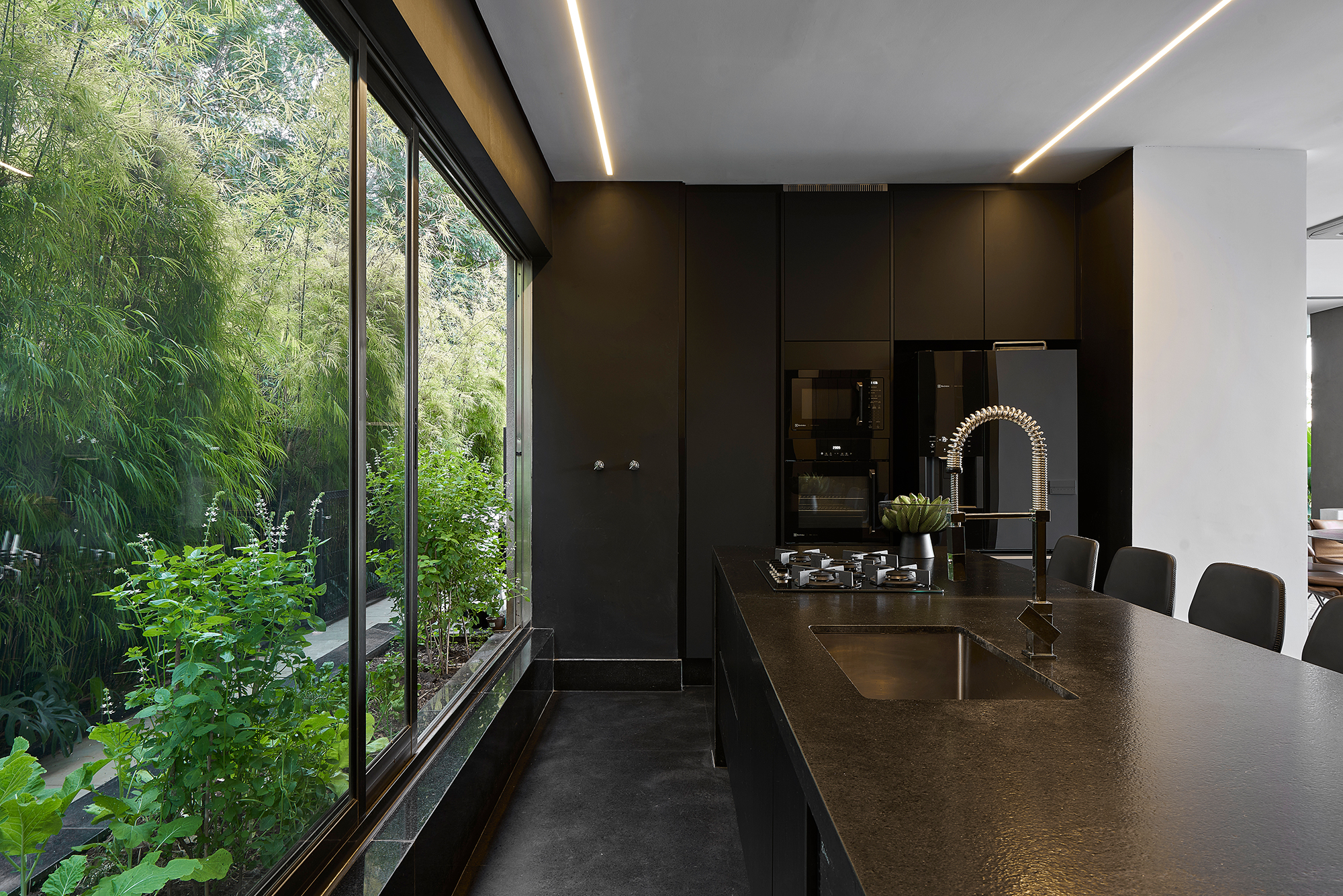 Em Minas Gerais, casa de 620 m² ganha projeto que valoriza a área externa. Projeto de Junior Piacesi. Na foto, cozinha com ilha, marcenaria preta e jardim.