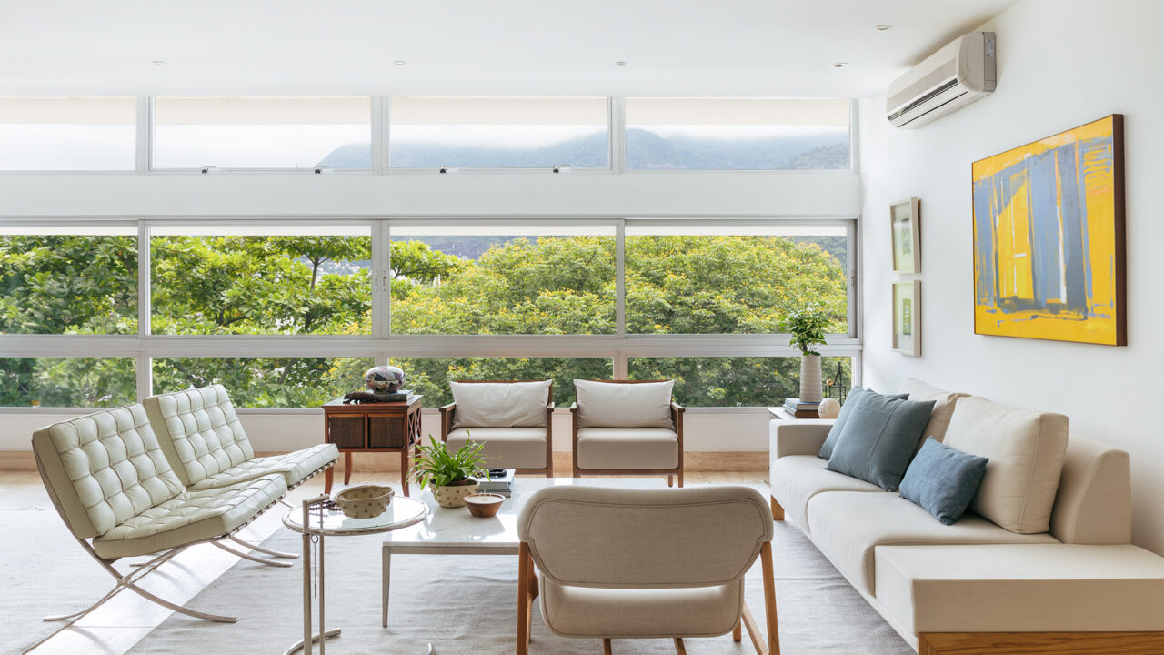 A natureza carioca circunda todo este apartamento de 245 m². Projeto de Vivian Reimers. Na foto, sala com vista para as árvores, quadros e sofás.