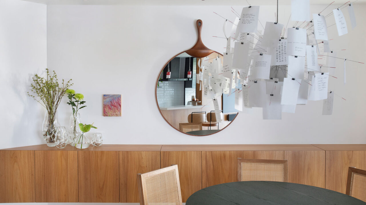 Grande painel de madeira emoldura a cozinha deste apê de 90 m² no Leblon. Projeto de Mar Arquitetura. Na foto, sala de jantar com lustre, aparador, espelho e mesa.