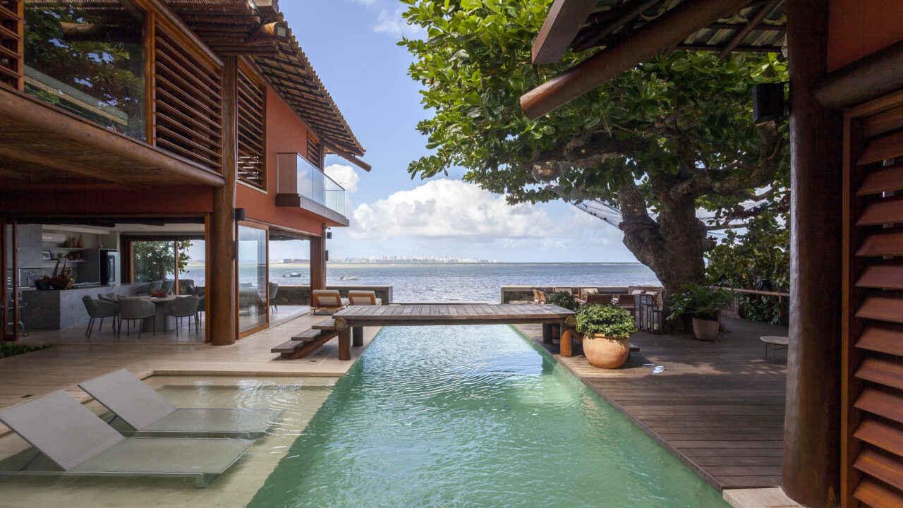 Piscina parece extensão do mar nesta casa assinada por David Bastos. Na foto, piscina com passarela no meio.