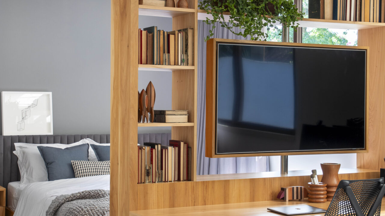 Em aclive, casa de estrutura metálica é erguida acima do nível da rua. Projeto de PKB Arquitetura. Na foto, quarto com tv giratória e home office.