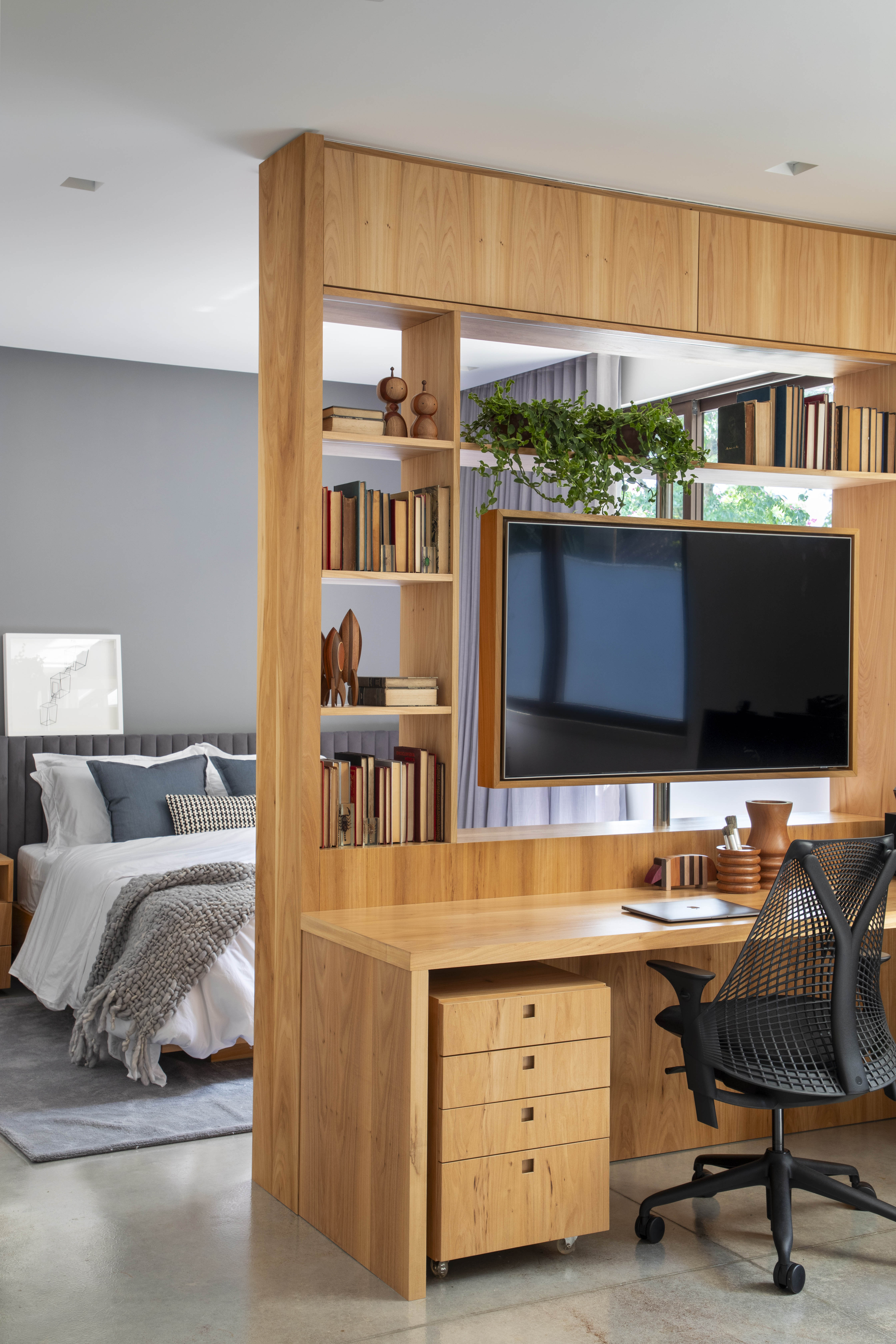 Em aclive, casa de estrutura metálica é erguida acima do nível da rua. Projeto de PKB Arquitetura. Na foto, quarto com tv giratória e home office.