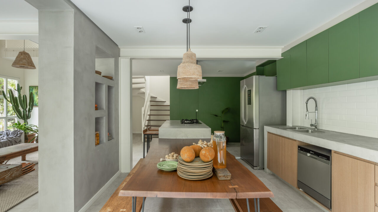 Casa de praia repleta de plantas se integra à mata nativa do entorno. Projeto de Ricardo Abreu. Na foto, cozinha com mesa de madeira e marcenaria verde.