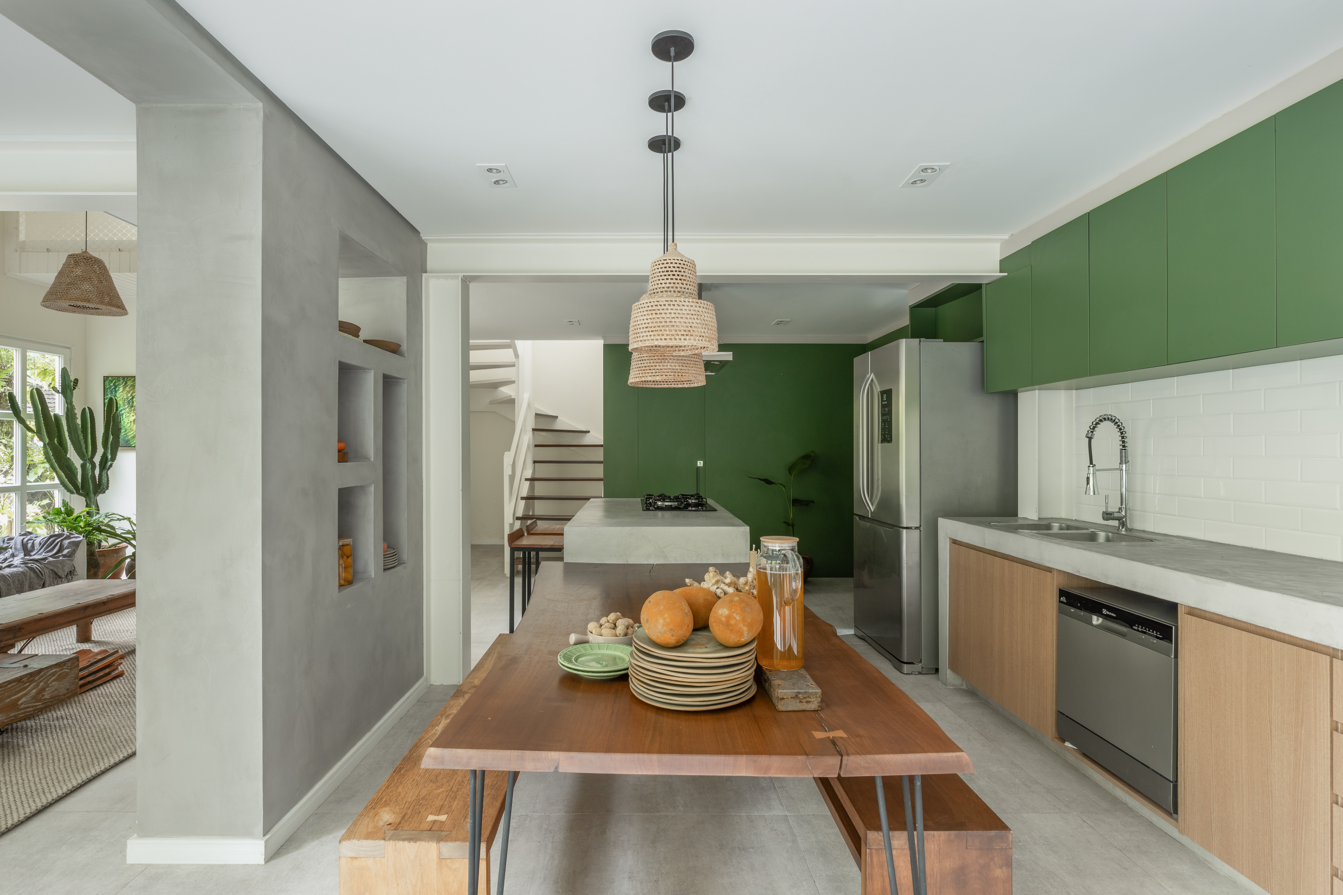 Casa de praia repleta de plantas se integra à mata nativa do entorno. Projeto de Ricardo Abreu. Na foto, cozinha com mesa de madeira e marcenaria verde.