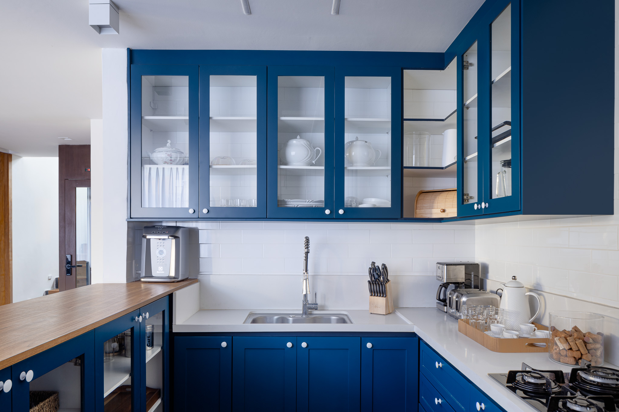 Casa na serra ganha anexo com parede de pedra em projeto de Rafael Mirza. Na foto, cozinha com marcenaria azul e subway tiles.