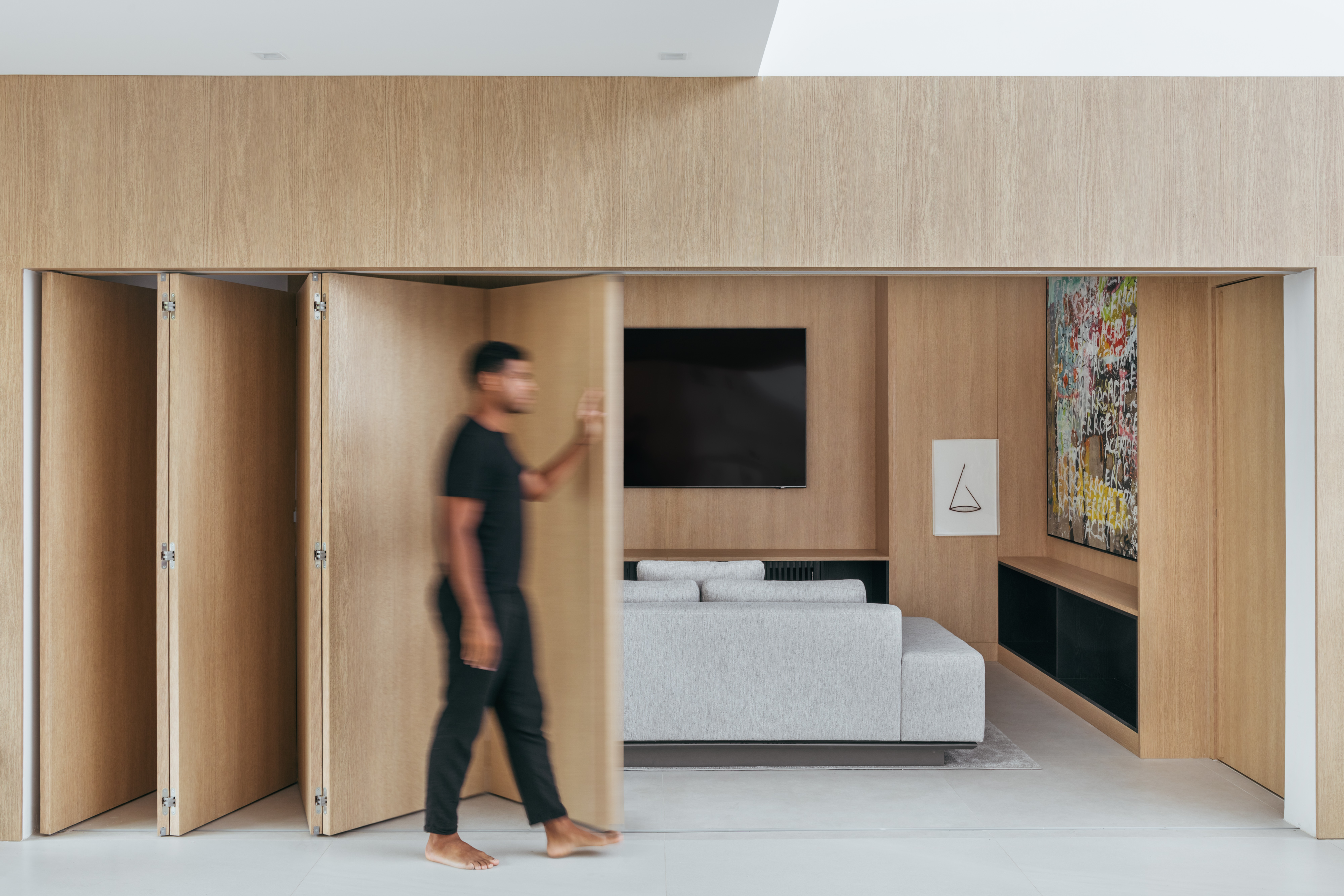 Conheça a casa de 750 m² do jogador de futebol André Balada. Projeto de Tom Castro. Na foto, sala de TV com porta camarão e parede de madeira.