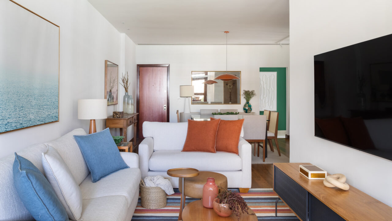 Apartamento à beira-mar ganha cara de casa com cozinha verde. Projeto de Vivian Reimers. Na foto, sala de estar com tapete listrado, tv e quadros.