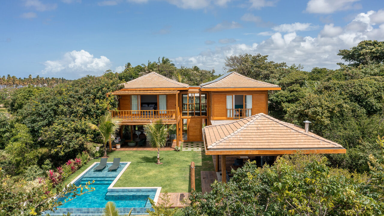 Casa na praia se integra à natureza com venezianas móveis na fachada. Projeto de Sidney Quintela. Na foto, fachada da casa com jardim e piscina.