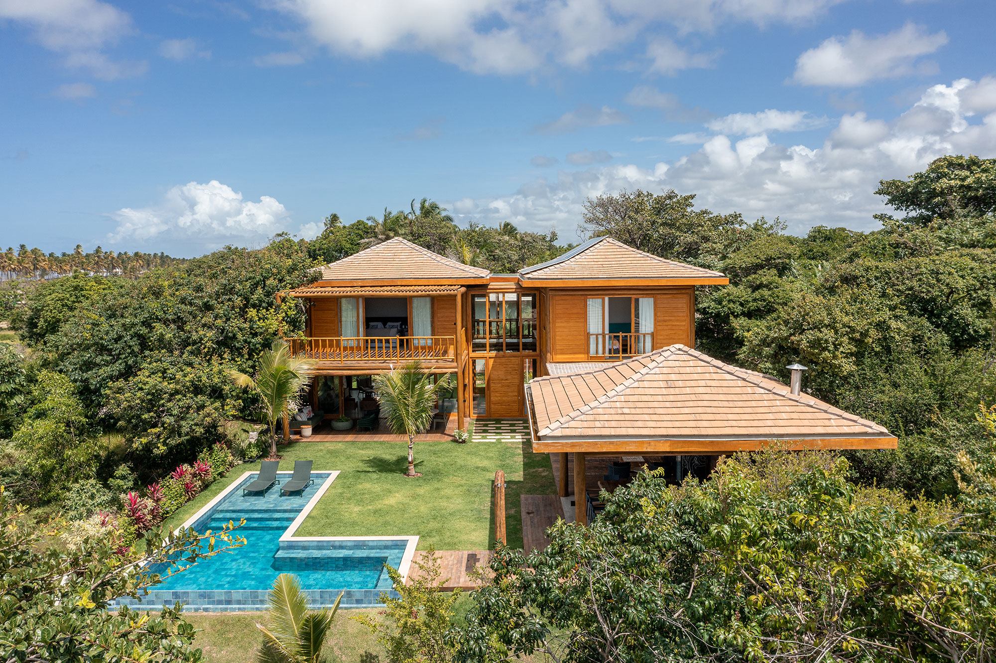 Casa na praia se integra à natureza com venezianas móveis na fachada. Projeto de Sidney Quintela. Na foto, fachada da casa com jardim e piscina.