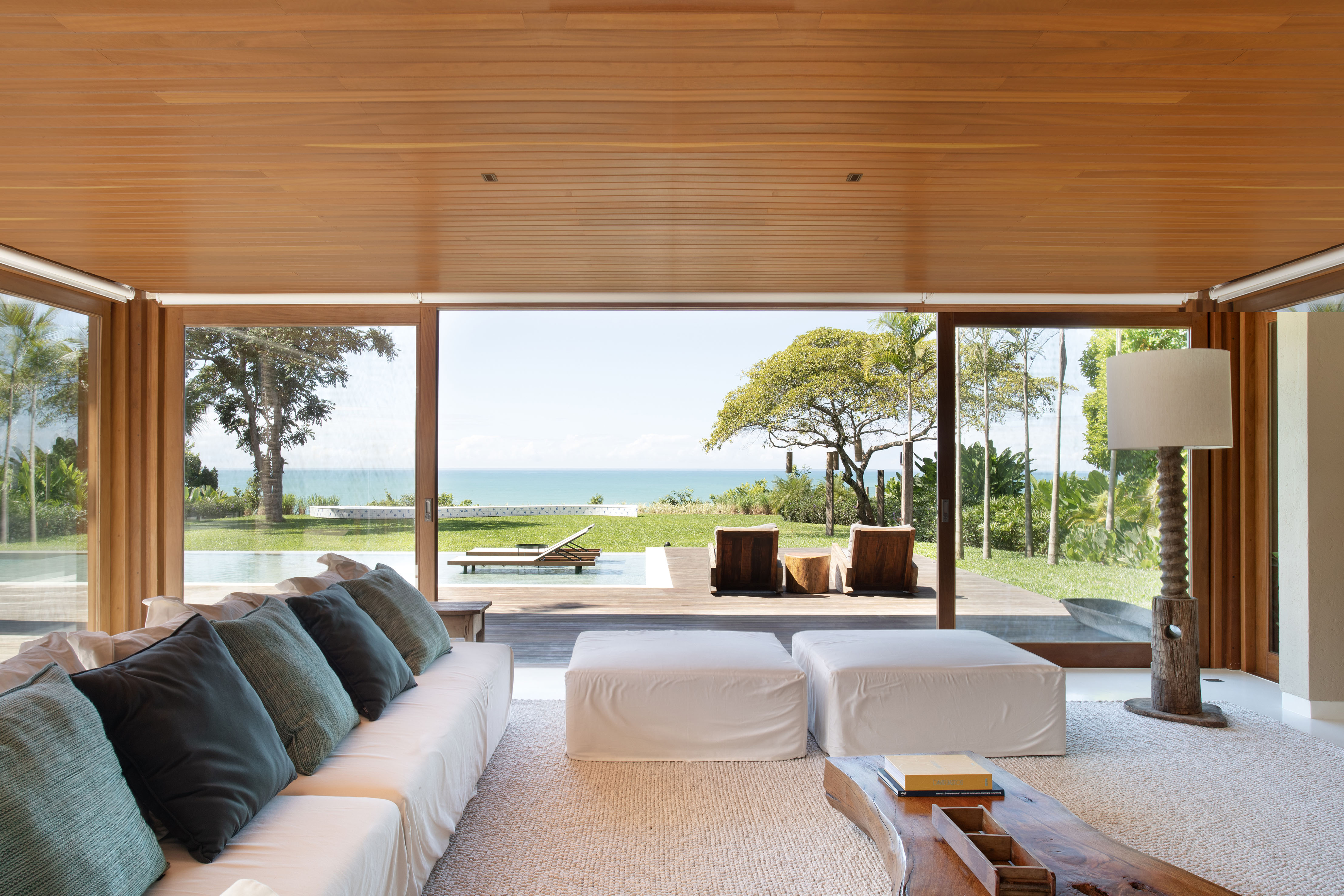 Feita do zero, casa de praia enquadra o mar em suas aberturas. Projeto de David Bastos. Na foto, sala com varanda e piscina.
