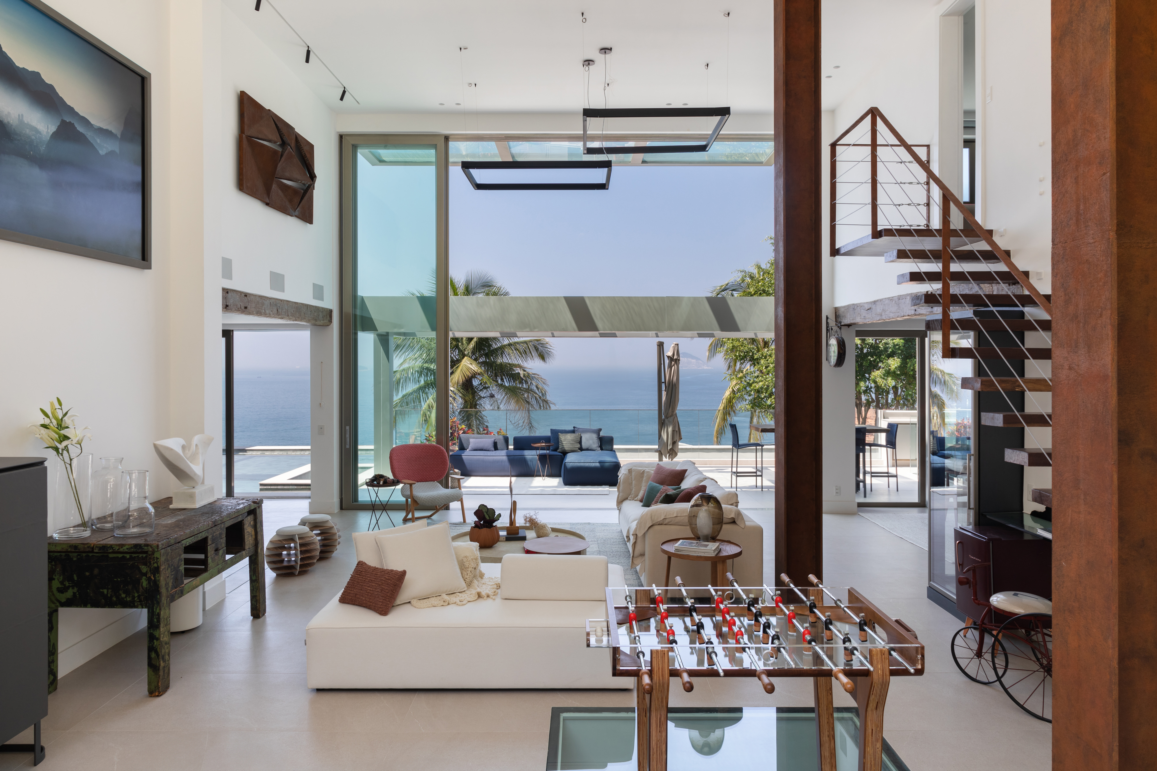 Em frente ao mar, casa une suíte-loft, TV escondida e jardim de esculturas. Projeto de Ketlein Amorim. Na foto, sala de estar com escada e vista para o mar.