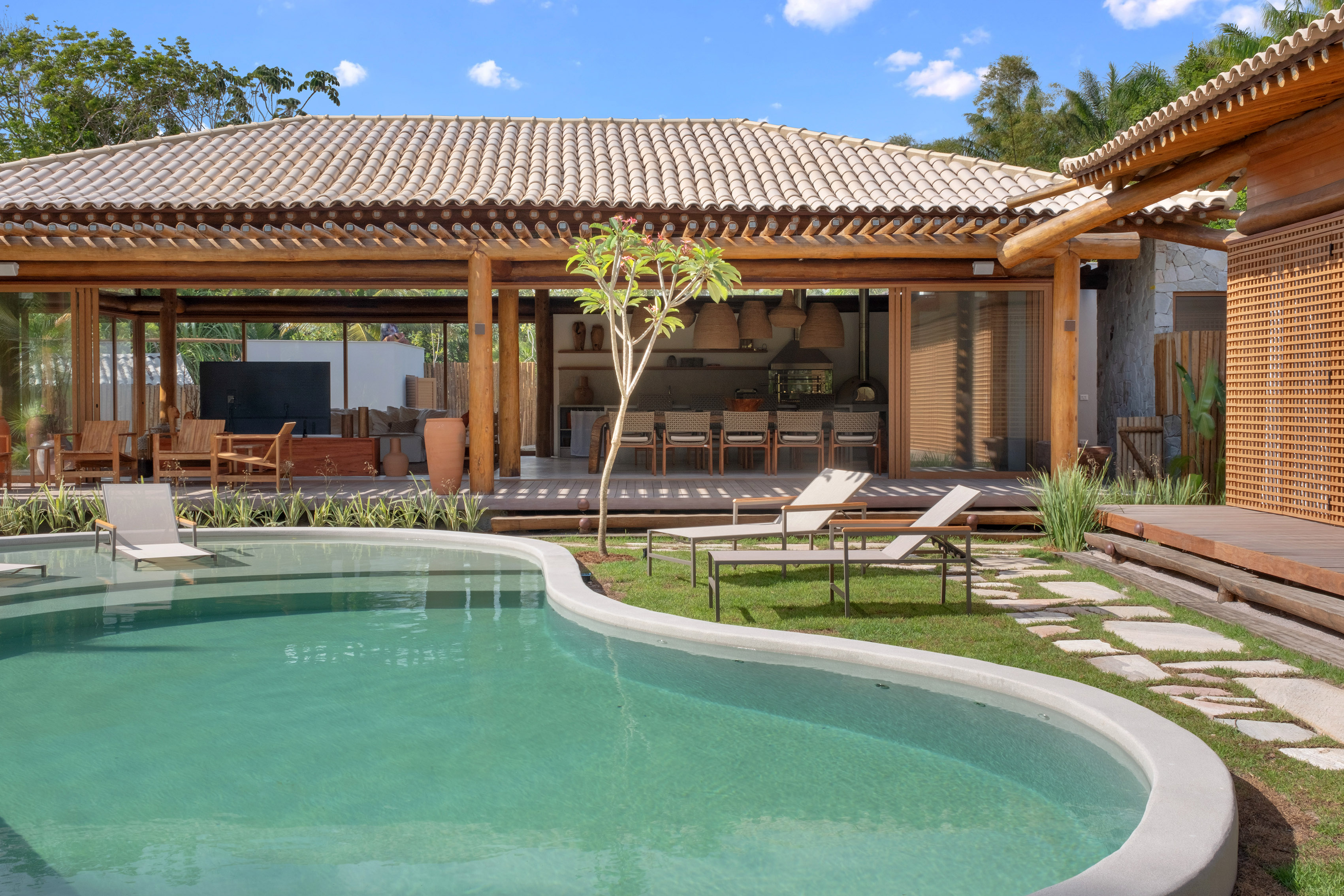 Casa de praia com estrutura de madeira possui piscina orgânica e redário. Projeto de David Bastos. Na foto, jardim com piscina, redes e jardim.