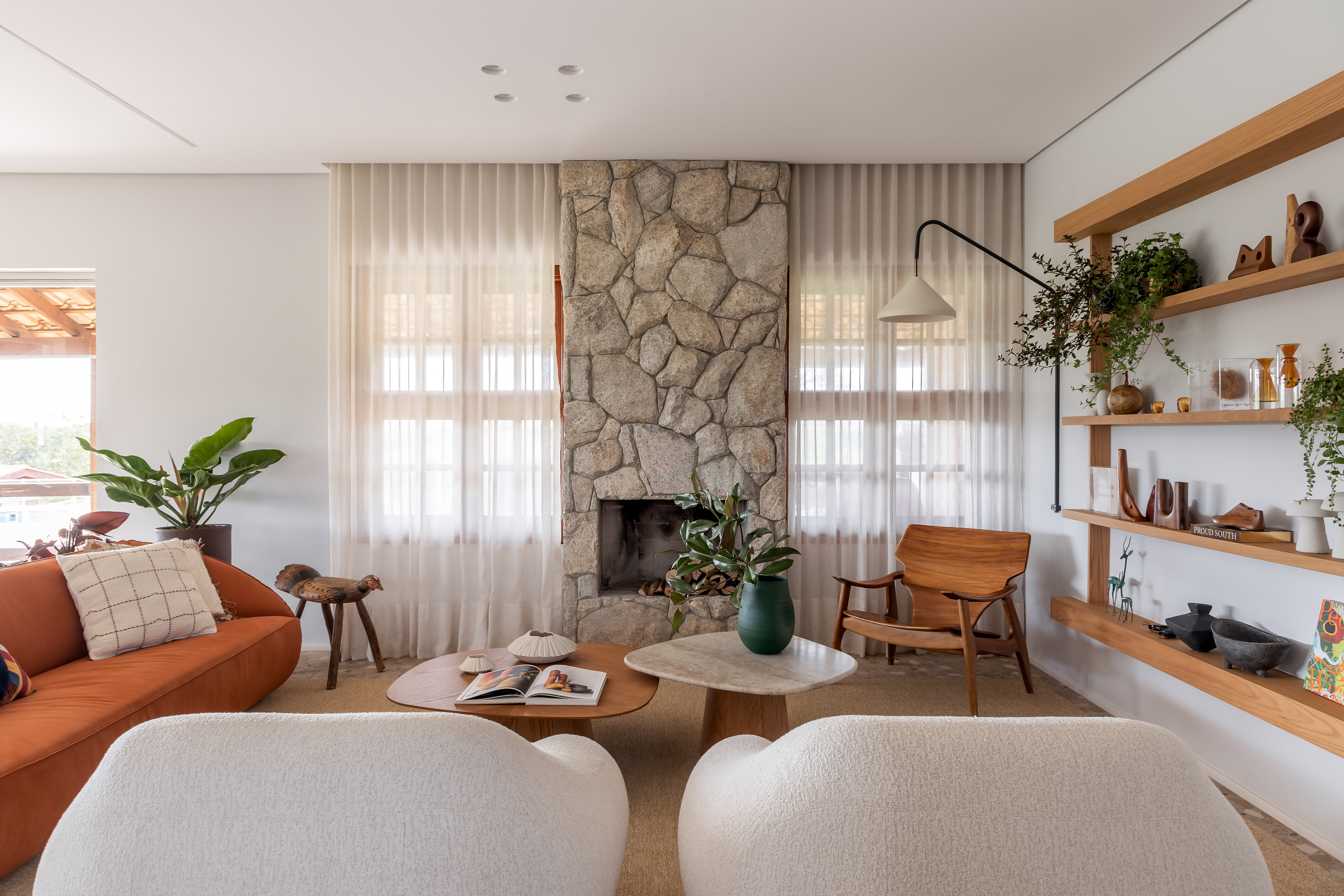 Casa de veraneio se transforma em lar definitivo da família. Projeto de Beatriz Quinelato. Na foto, sala com parede de pedra, lareira e prateleiras.