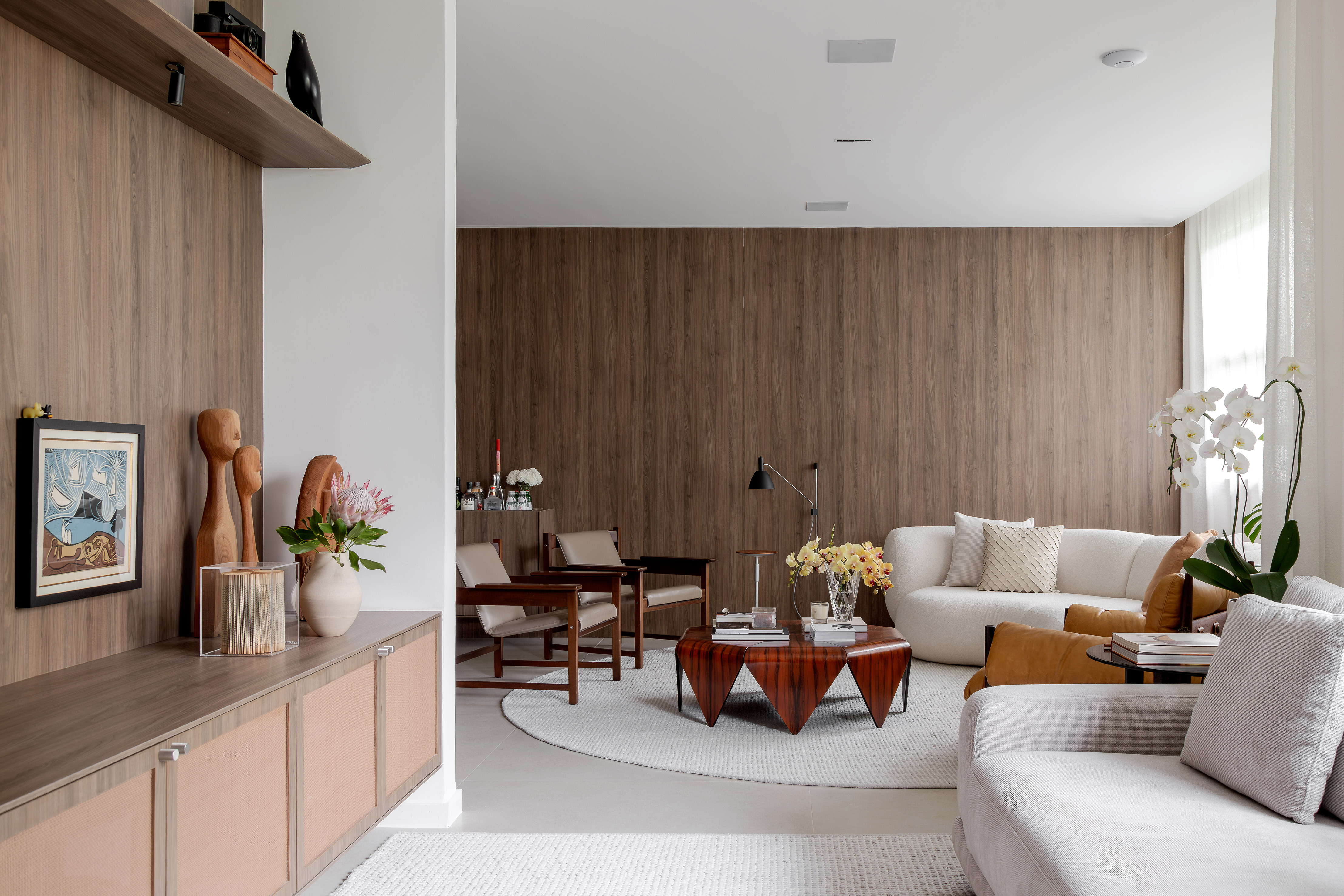 Conheça o apartamento dos arquitetos Carol Freitas e Fabio Bouillet. Na foto, sala de estar com sofá curvo, poltronas e mesa de centro.