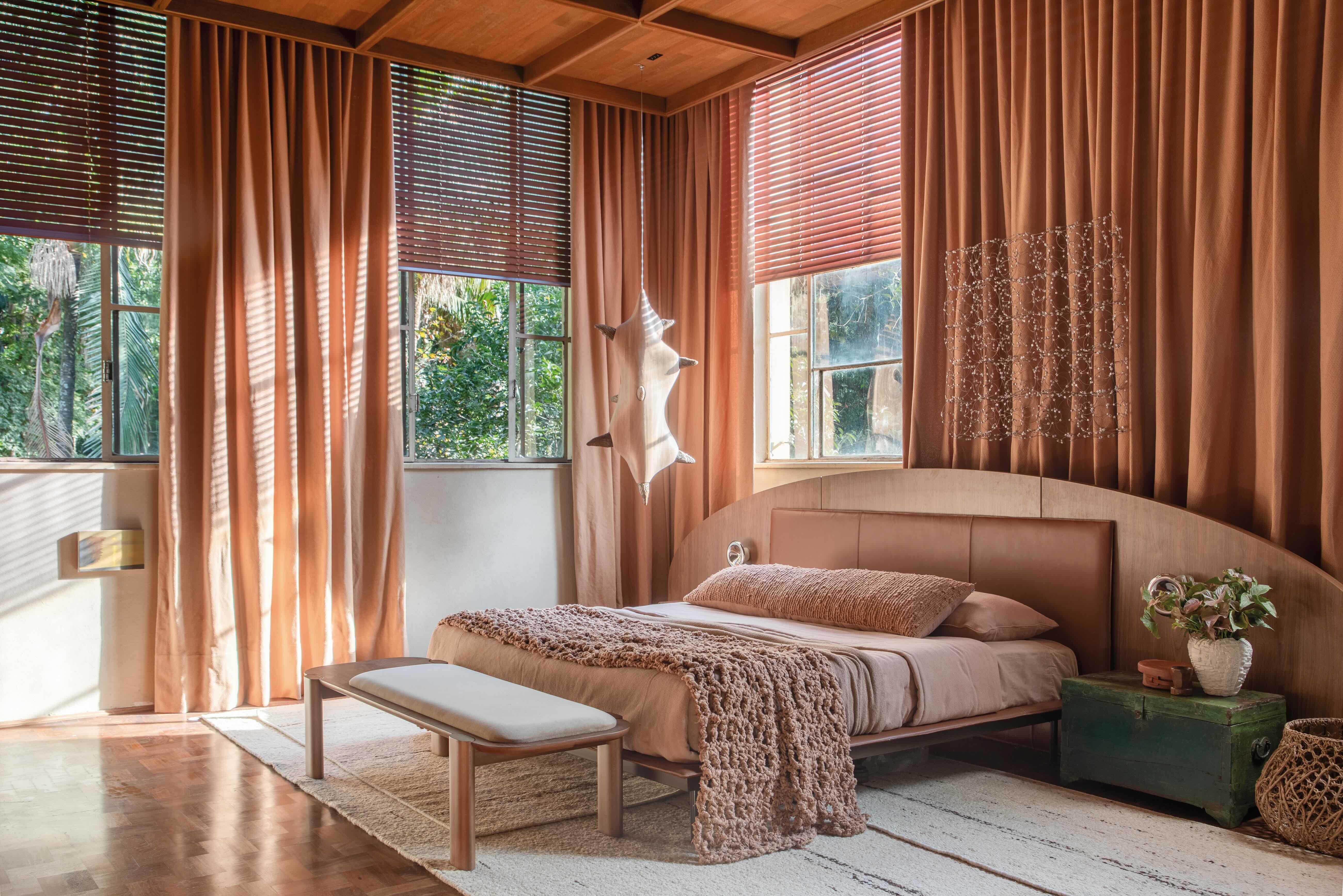 Beatriz Quinelato Arquitetura - Sopro. Texturas naturais, cores terrosas e formas suaves respondem pelo jeito caloroso desta suíte máster de 45 m², idealizada como refúgio urbano sob a ótica de um estilo de vida simples e consciente. Entre os materiais, distinguem-se as pedras brutas usadas na bancada do banheiro, na área do boxe e na base da lareira, além do forro de madeira com trama quadriculada. A cama está rodeada de arte: do teto pende a curiosa escultura Seres, de madeira e cerâmica, assinada por André Ferri. Rente à cortina, vê-se Palavra Cruzada, um delicado emaranhado de resina e cobre, trabalho de Luiz Hermano.