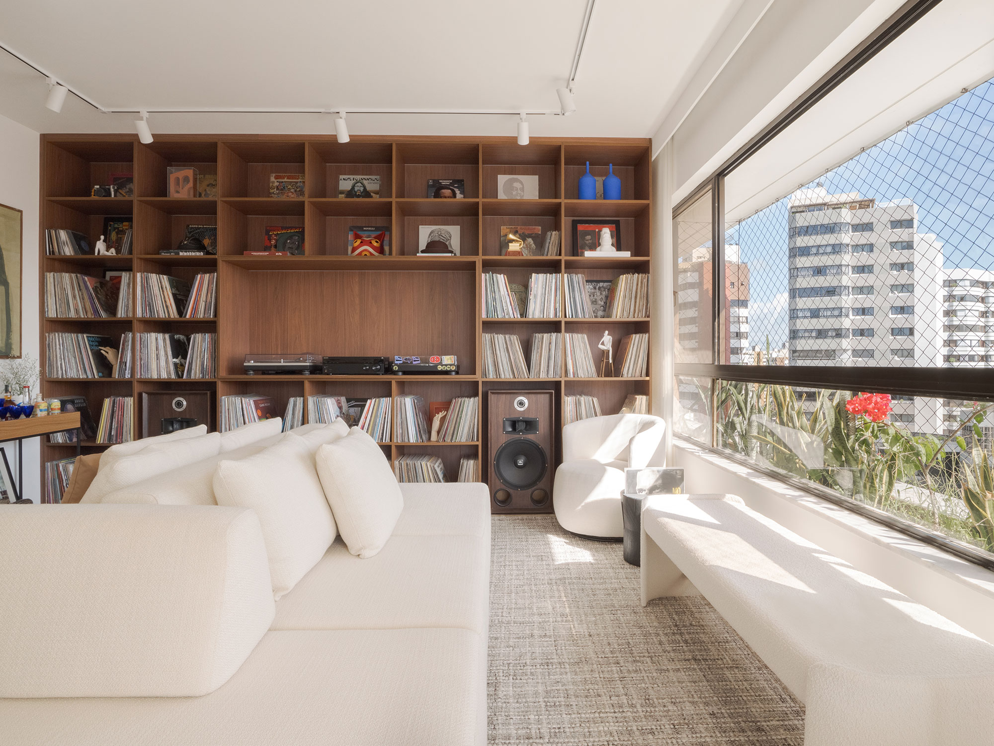 Estante expõe coleção de vinis e ganha protagonismo neste projeto. Projeto de Neto Cunha. Na foto, sala com estante de vinis, banco e sofá ilha.
